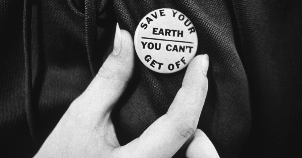 یک دست نزدیک یک دکمه روز زمین را نگه میدارد که در ان نوشته شده است :‌"زمین خود را نجات ده شما نمیتوانید پیاده شوید"